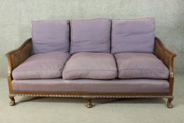 An early 20th century three seater bergère sofa, with a caned back and arms, upholstered in a deep