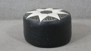 A Middle Eastern pouffe, of circular form, black with an ivory coloured flowerhead top, decorated