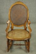 A fruitwood rocking chair, the oval back, and the seat both caned, on turned legs joined by