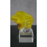 A art glass figure of a head with flowing yellow hair mounted on a clear glass block. H.19 W.8.5 D.