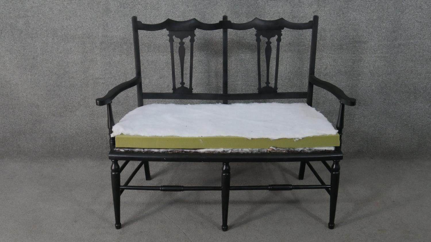 An ebonised wood two seater settee, the double chair back with pierced splats and open arms. H.90