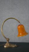 An Edwardian brass desk lamp, with an orange glass shade, on a curved stem, with a heart shaped