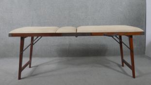 A mid 20th century teak folding therapist's massage table, upholstered in ivory faux leather. H.73