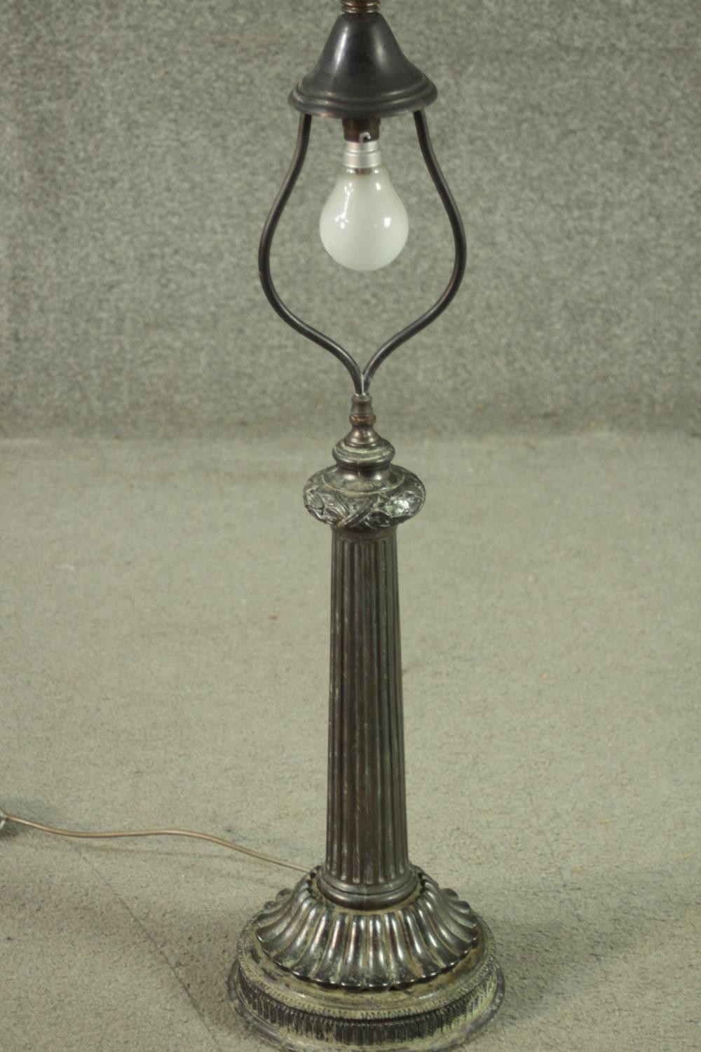 A vintage metal table lamp with ribbon and acorn decoration above a tapering fluted column on