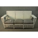 A white painted rattan garden three seater sofa, of woven construction, with a black and white