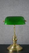 A brass banker's desk lamp, with a green glass shade, on a curved stem and a circular footed base.