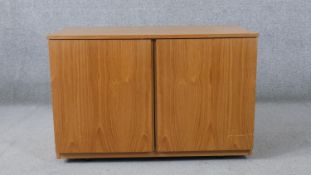 A teak music cabinet, with two doors, enclosing storage for vinyl records, on castors. H.55 W.85 D.