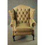 A contemporary Thomas Lloyd cream leather wing back armchair, with a buttoneb back, and scrolling