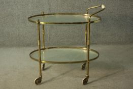A circa 1950s brass oval drinks trolley, of two tiers, with textured glass, on castors. H.70 W.68