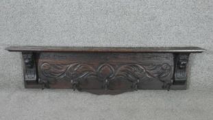 A carved oak wall mounted coat rack, with a shelf over a carved acanthus leaf panel with lion head