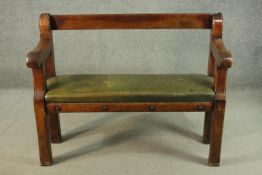 A 19th century ecclesiastical bench, with a bar back and open arms, over a green leather seat, on