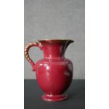 A vintage red glaze jug with twisted handle design with gilded detailing to the handles and starts