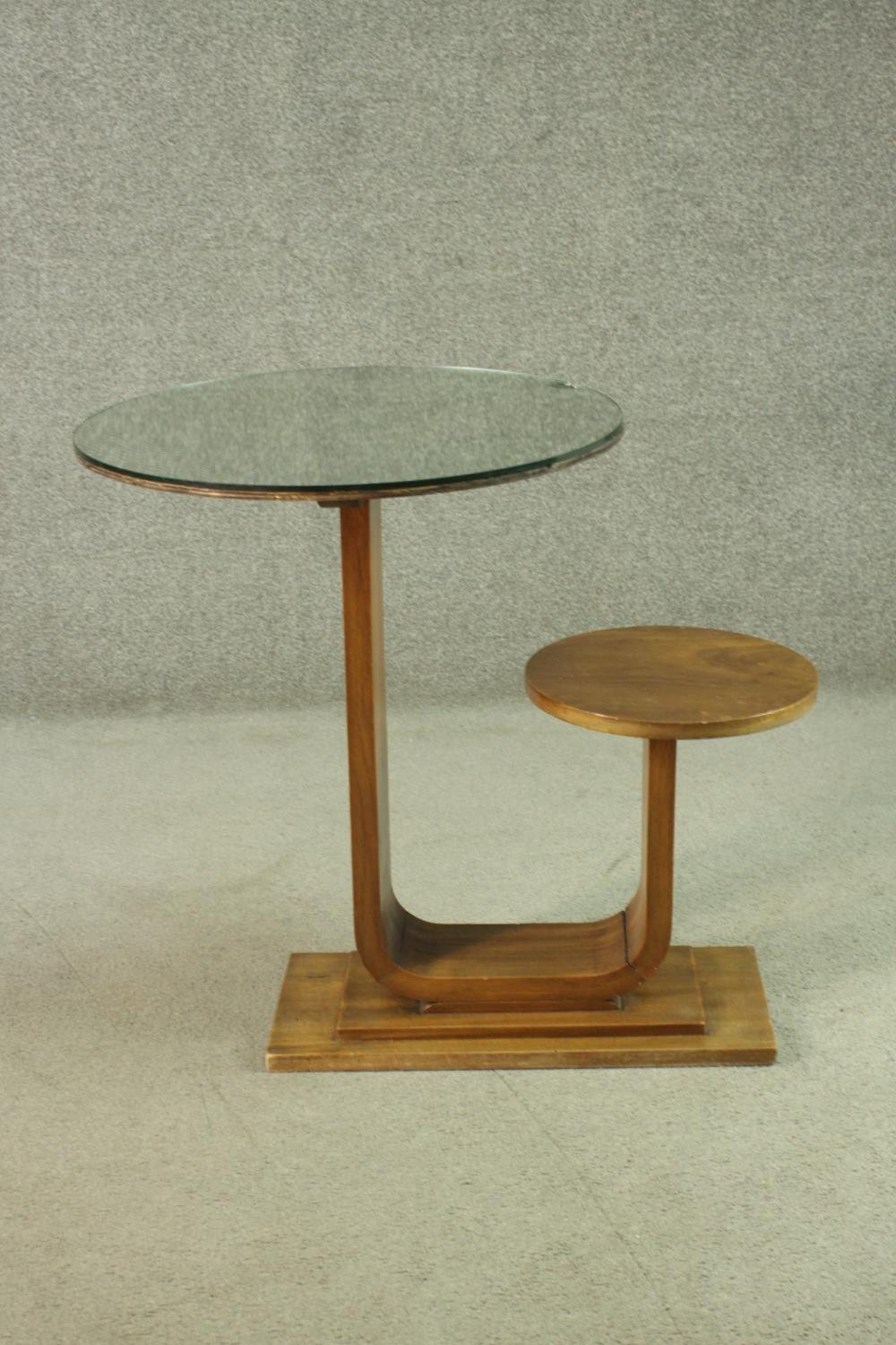 An Art Deco teak table and stool, with a circular glass table top, on a support which curves up to a