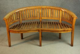 A contemporary serpentine teak garden bench, with a curved back, the back and seat of slatted