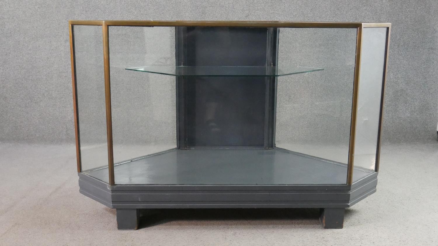 A mid 20th century shop corner display cabinet, glazed, with brass edges, enclosing a single