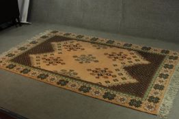 A Chinese woollen carpet with central hooked medallions on a sand ground within a flowerhead border.