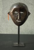 A carved African tribal mask with beaded earring on a metal display stand. H.40cm.