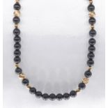 An obsidian and 14k gold bead necklace. Strung with fifty three round polished obsidian beads