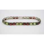 A silver peridot and garnet set line bracelet. Set with twelve oval mixed cut peridots in open