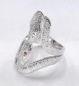 A contemporary silver and cubic zirconia double kissing snake ring. The eyes set with orange cubic