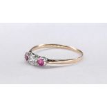 A yellow and white metal ruby and diamond three stone ring. Set to centre is a round brilliant cut