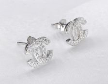 A pair of white metal (tests as silver) and cubic zirconia designer logo earrings. Secure posts to