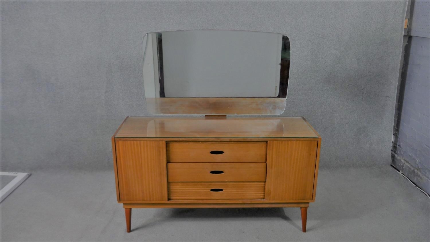 A circa 1960s teak dressing table, with a frameless mirror over three short drawers flanked by