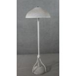 A white painted Lloyd loom wicker standard lamp, with a circular wicker shade, on tripod legs with a
