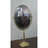 A large 20th century brass swing frame toilet mirror, with an oval mirror plate, on a circular base.