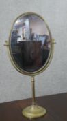 A large 20th century brass swing frame toilet mirror, with an oval mirror plate, on a circular base.
