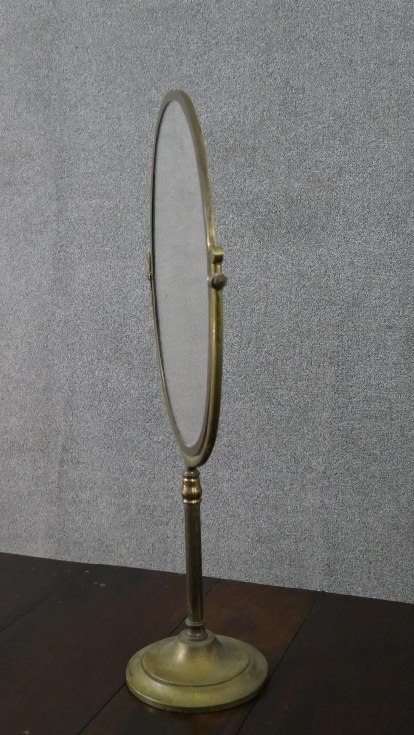 A large 20th century brass swing frame toilet mirror, with an oval mirror plate, on a circular base. - Image 2 of 6