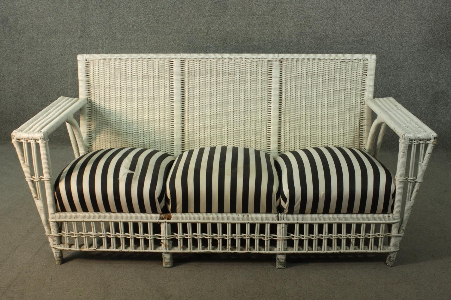 A white painted rattan garden three seater sofa, of woven construction, with a black and white