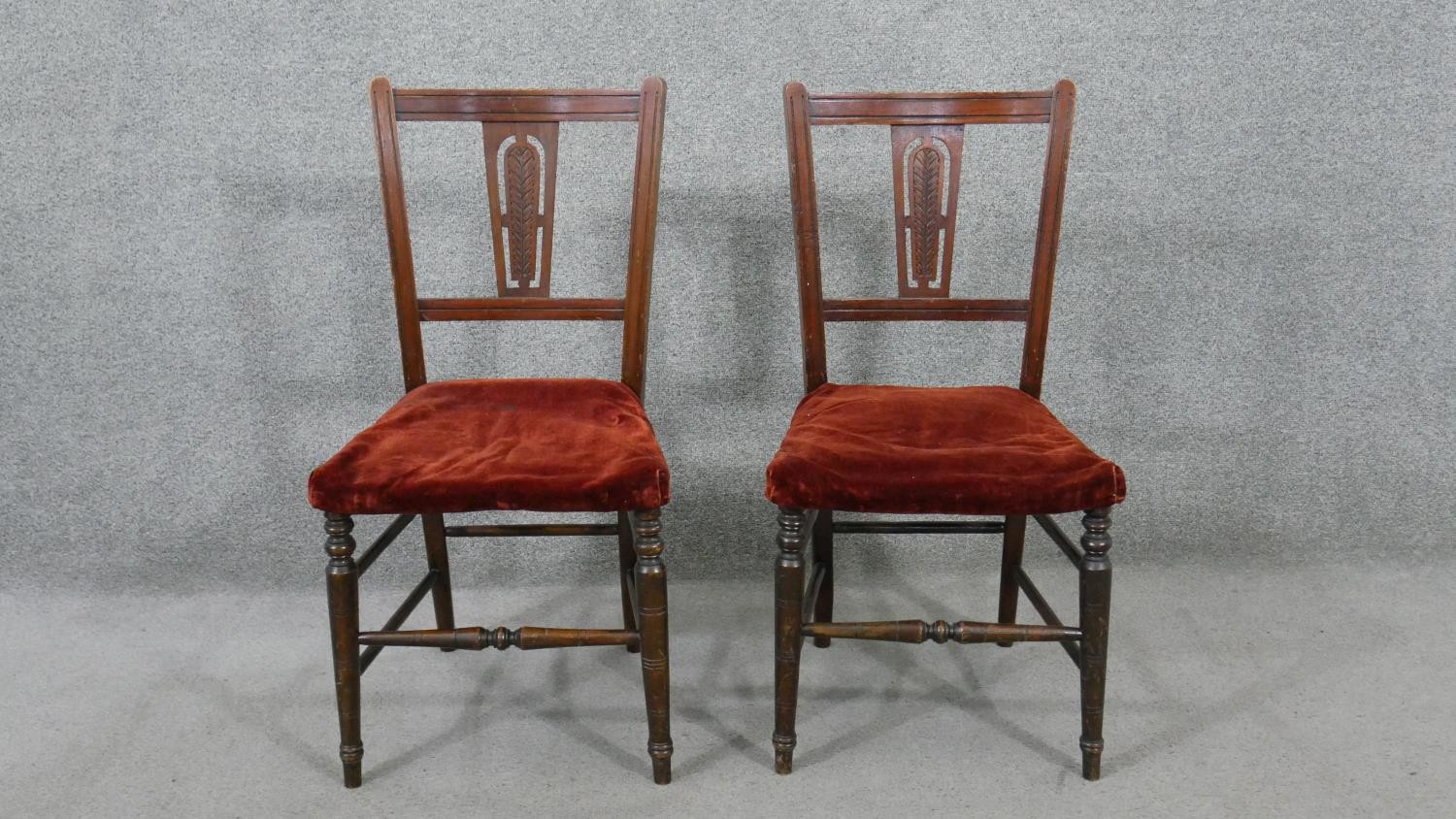 A pair of Edwardian walnut side chairs, the back with a carved foliate splat, over a red velour