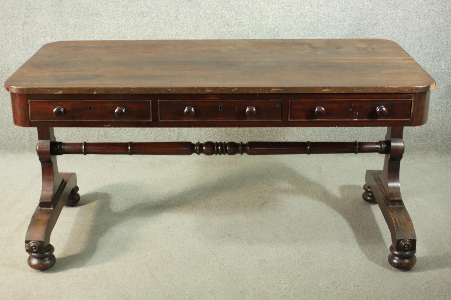 A Victorian mahogany library table, with three short drawers, over end supports joined by a turned