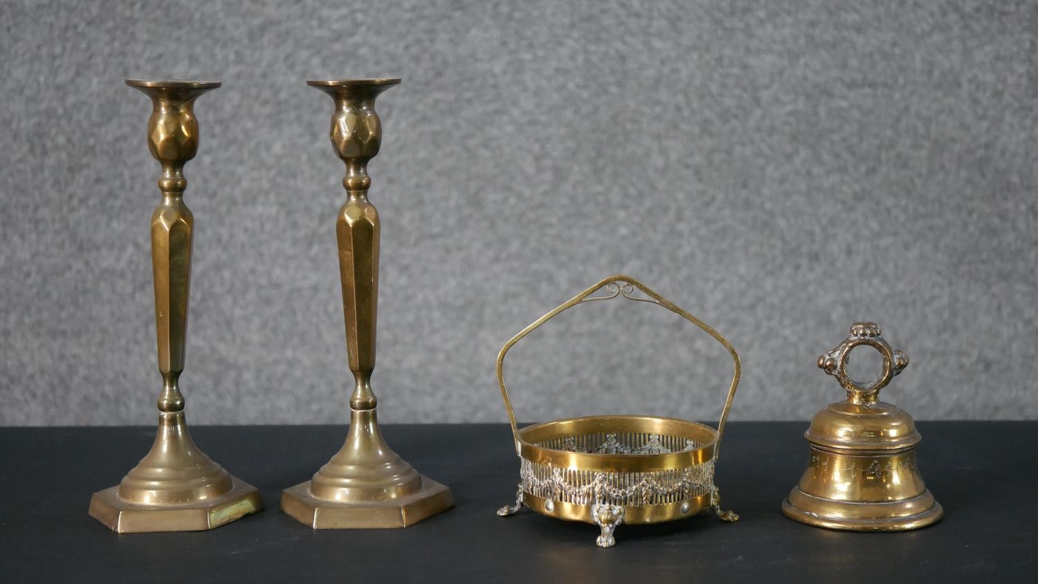 A collection of brass, including a pair of brass candlesticks with faceted design, a brass hand bell