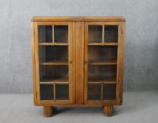 An early 20th century oak display cabinet, with a pair of glazed doors, enclosing shelves, on reeded