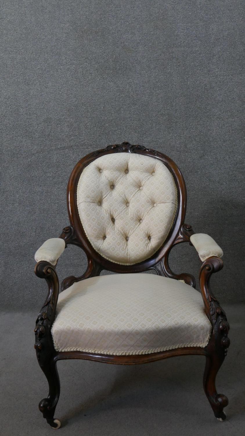 A Victorian walnut open armchair, upholstered in patterned ivory fabric, with an oval buttoned back,