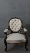 A Victorian walnut open armchair, upholstered in patterned ivory fabric, with an oval buttoned back,