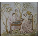 A framed and glazed 19th century silk embroidery of three people playing backgammon in a garden with