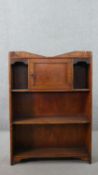 A circa 1900 oak open bookcase, with a shaped three quarter gallery over a single cupboard door