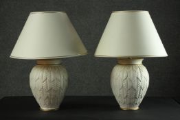 A pair of table lamps, the ivory coloured ovoid body with allover leaf design, parcel gilt, with