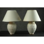 A pair of table lamps, the ivory coloured ovoid body with allover leaf design, parcel gilt, with