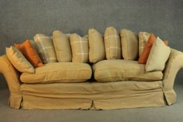 A contemporary three seater sofa, upholstered in ochre fabric, with scrolling arms and a selection