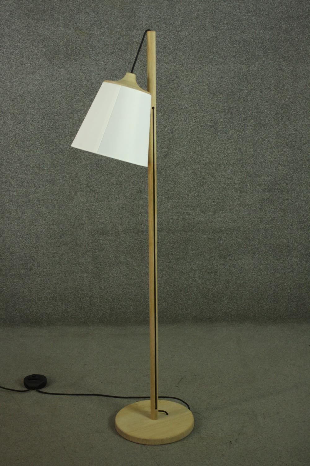 A contemporary light oak standard lamp, the white shade hanging from a cylindrical stem, on a
