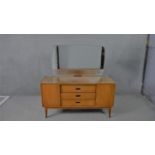 A circa 1960s teak dressing table, with a frameless mirror over three short drawers flanked by