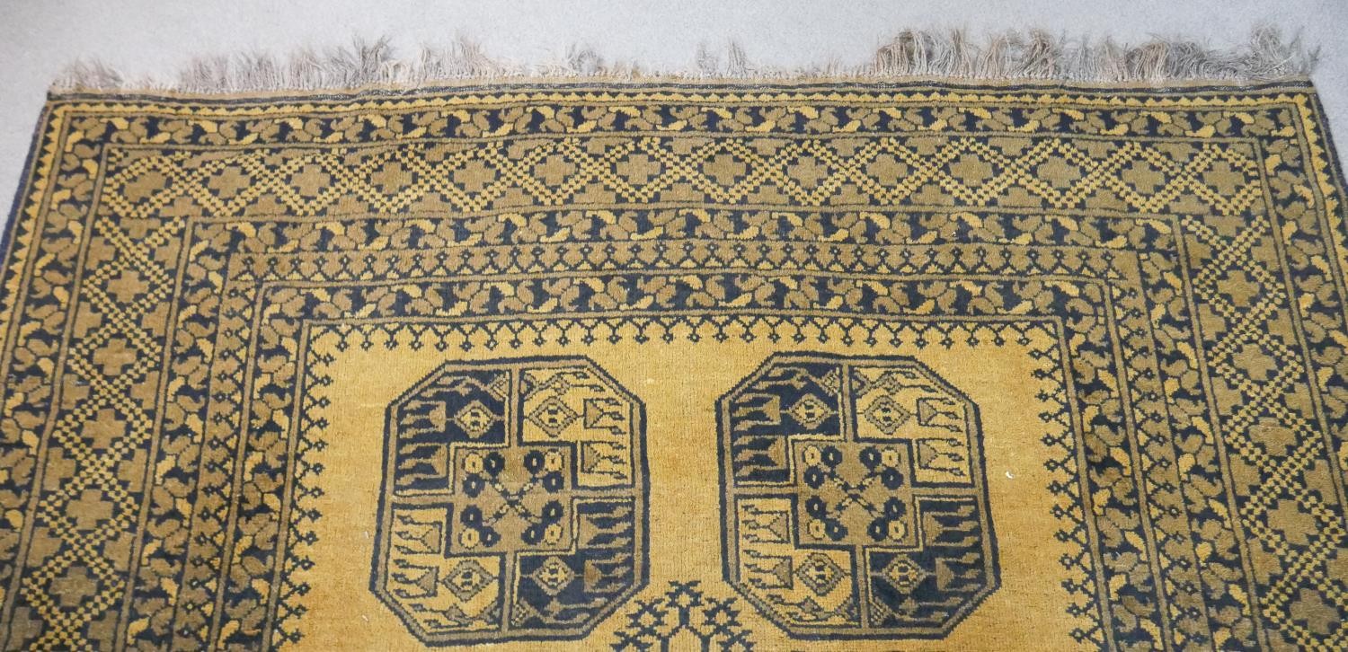A hand made Afghan carpet with repeating gul medallions on a gold ground contained within multiple - Image 4 of 7