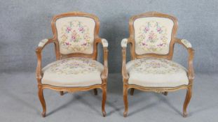 A pair of Louis XV style French walnut fauteuil armchairs, the needlepoint upholstery with foliate