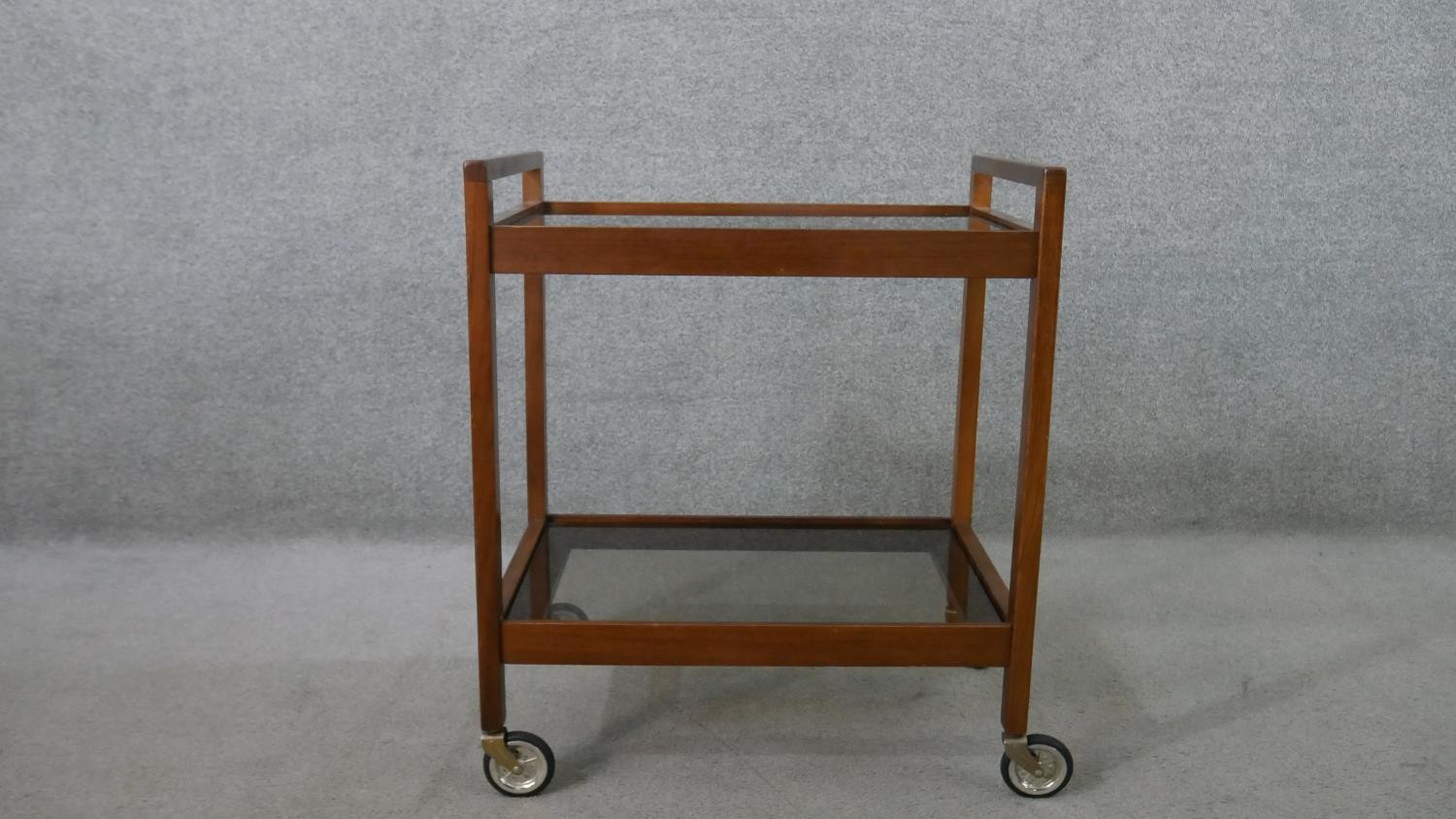 A circa 1960s mahogany drinks trolley, with two tiers of clear plate glass, on castors. H.72 W.62