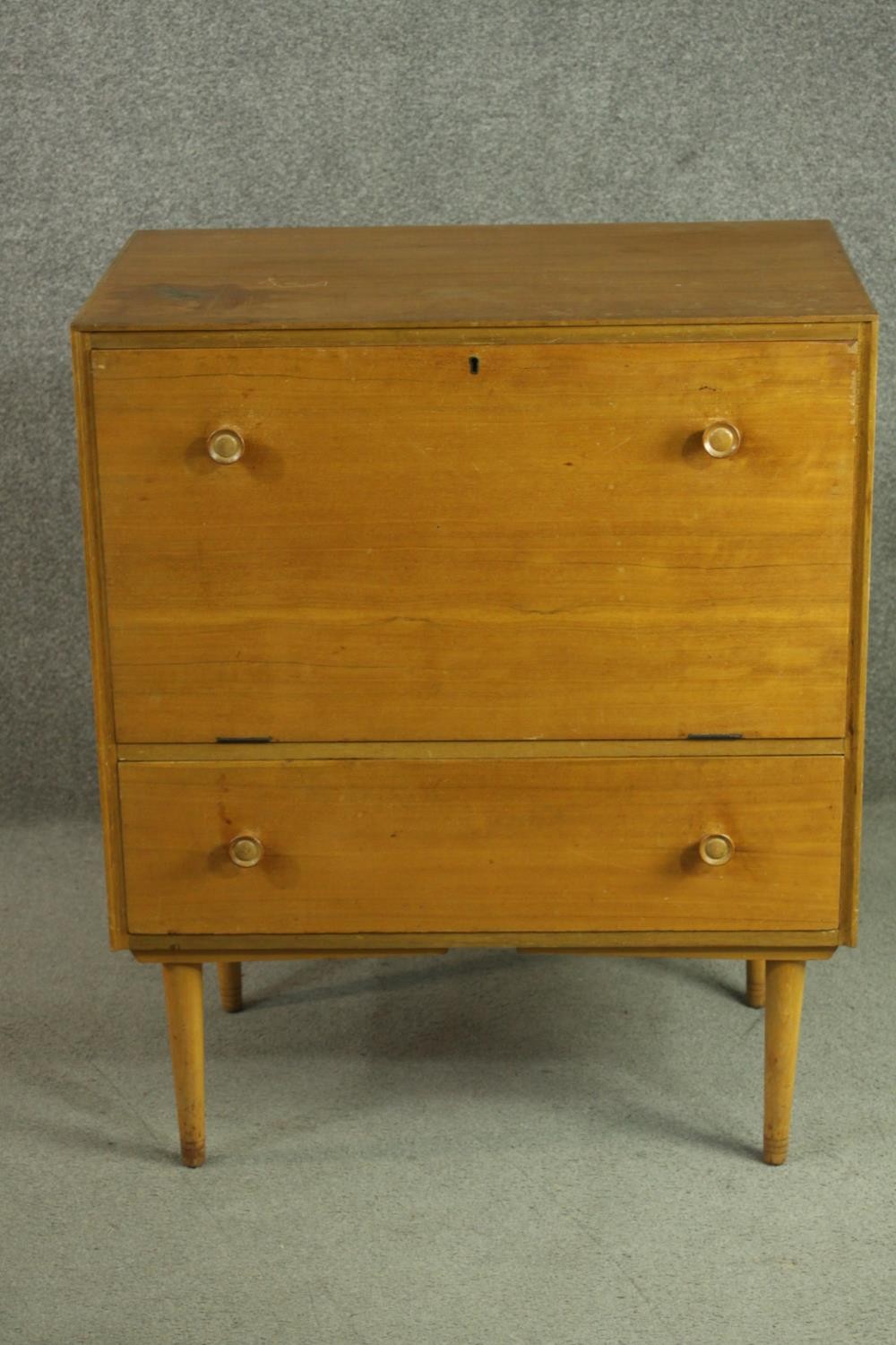 A circa 1950s teak cabinet, with a fall front enclosing a pull-out section, over a single drawer, on