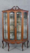 An Edwardian mahogany display cabinet, with a swan neck pediment, over a pair of bevelled glass